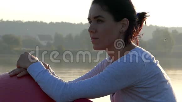 一个年轻的女人坐在湖畔的一个健身球上视频的预览图