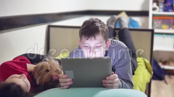 狗宠物舔男孩有趣的友谊男孩和女孩躺在床上玩平板电脑青少年社会视频的预览图