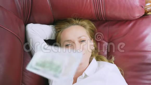 被动收入的概念幸福的女人躺在沙发上微笑在她不断下降的美元之上4k特写视频的预览图
