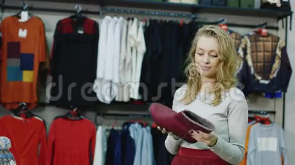 一个有魅力的年轻女人在服装店里选择温暖的冬鞋微笑看着红色的靴子视频的预览图