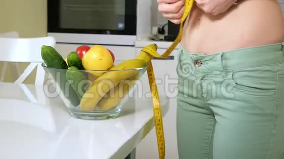 苗条的女人在一盘水果和蔬菜的背景下测量臀部这是一种健康的生活方式视频的预览图
