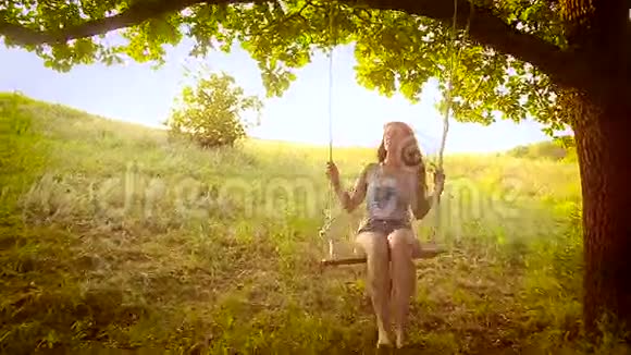 快乐的女孩在公园里荡秋千在树上荡秋千视频的预览图