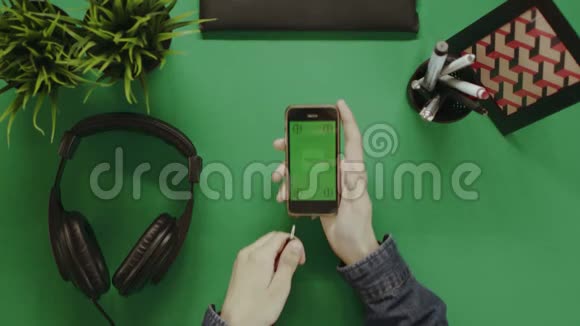 头顶拍摄的男子使用智能手机绿色屏幕和耳机视频的预览图