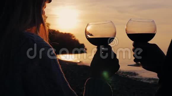 男人和女人的手拿着酒杯在夕阳西下的海面上喝酒视频的预览图