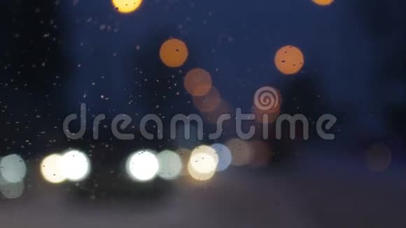 城市的雪夜挡风玻璃窗户上的水滴汽车灯的焦点背景视频的预览图