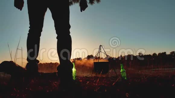 男子旅游舞蹈正坐在篝火晚会的大自然露营剪影阳光日落度假时的男性剪影视频的预览图
