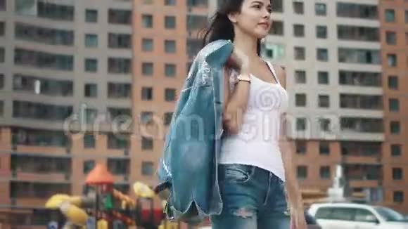 一个穿着白色T恤和牛仔裤的年轻女孩在高档现代化住宅之间视频的预览图