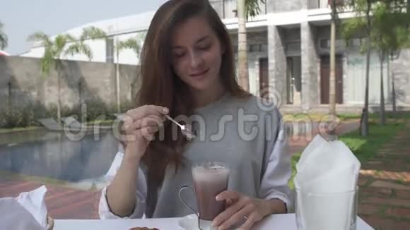 美丽的年轻女子在豪华别墅游泳池附近的早餐中搅动可可女性喝热巧克力视频的预览图