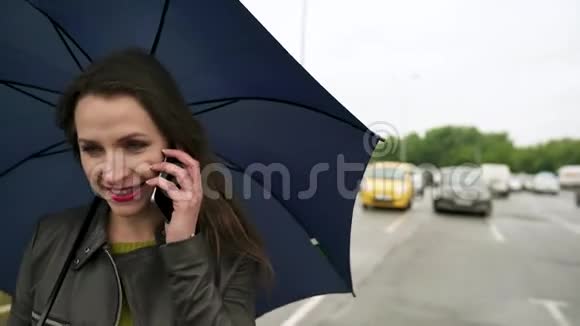 高加索女孩在伞下用智能手机说话视频的预览图