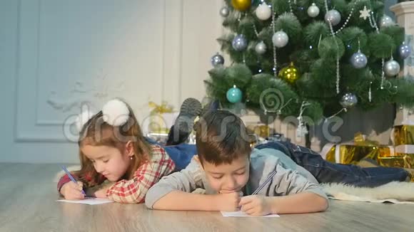 孩子们给圣诞老人写信对孩子们来说这是快乐的圣诞前夕小男孩和小女孩躺在地板上视频的预览图