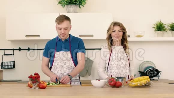 一对相爱的夫妇在厨房准备蔬菜和水果沙拉他们互相微笑玩耍视频的预览图