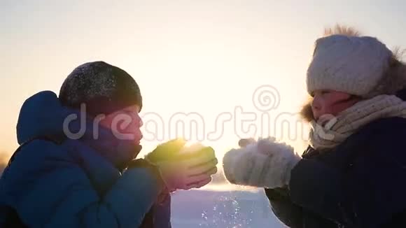 女孩和男孩在日落的背景下用手吹雪冬季雪景日落时间视频的预览图