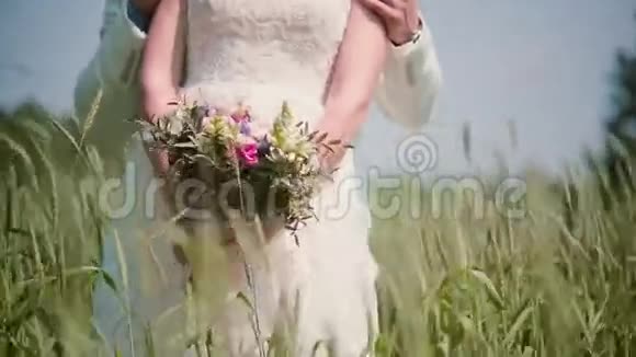 一位新娘和新郎站在麦田里手里捧着一束美丽的婚礼花束风中摇曳的圆锥体视频的预览图