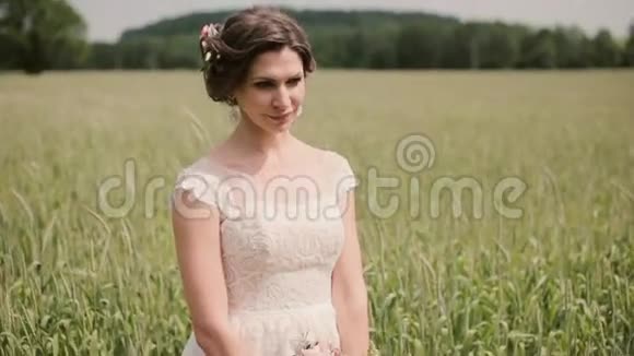 一个美丽的新娘穿着白色花边婚纱她手里拿着一束花站在麦田里视频的预览图