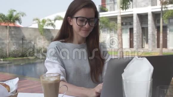 美丽的年轻女子在豪华别墅游泳池附近的笔记本电脑上工作女性在电脑上工作牛角面包和热巧克力视频的预览图