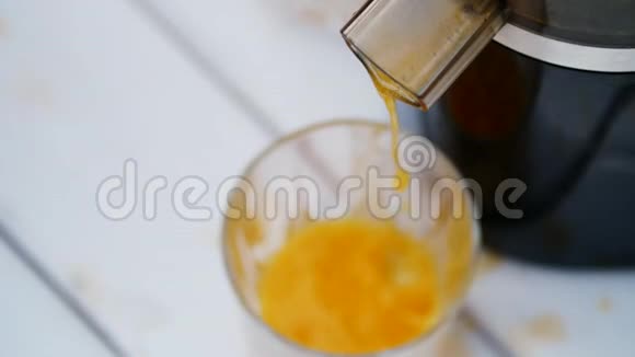 特写镜头从榨汁机流出新鲜榨出的橙汁倒入一杯从上面看视频的预览图