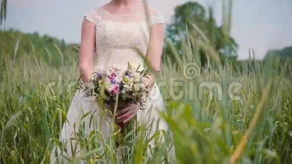 一位美丽的年轻新娘站在麦田里闻着她的结婚花束她穿着漂亮的花边婚纱视频的预览图
