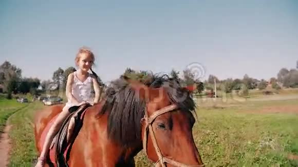 阳光明媚的一天一个快乐的小女孩骑着马在乡间的路上她在微笑玩得很开心慢点视频的预览图