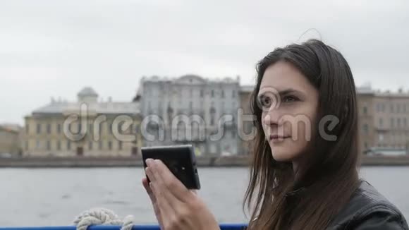 漂亮女孩在城市里拍照她很高兴微笑着用她的智能手机背景建筑慢的莫视频的预览图