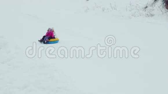 冬天的乐趣母亲和女儿骑着车走下一片白雪覆盖的山坡视频的预览图