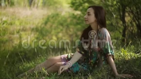 美丽的女孩坐在夏日公园的绿草中梦想视频的预览图