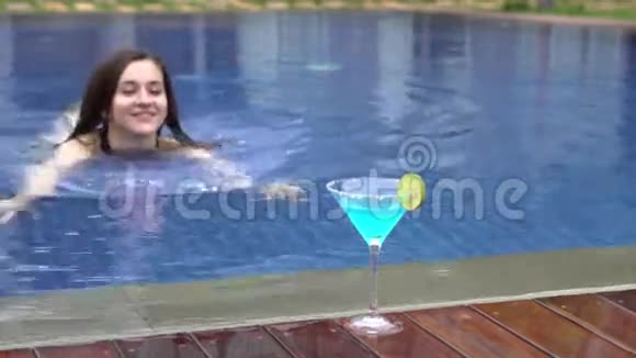 美丽的女孩在游泳池里游泳喝蓝色的coctail视频的预览图