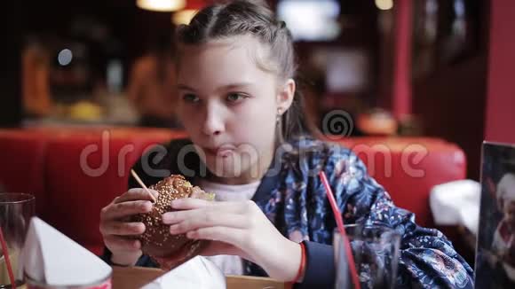小女孩高兴地在咖啡馆里吃汉堡快餐中的汉堡包和炸薯条视频的预览图