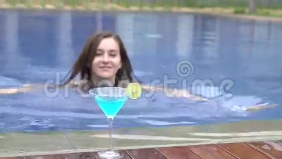 美丽的女孩在游泳池游泳喝蓝色的鸡尾酒玛格丽塔视频的预览图