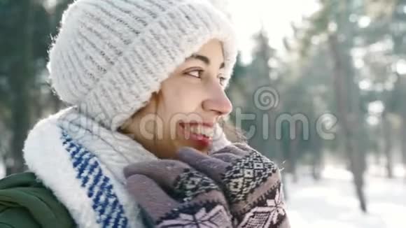 冬天的肖像滑稽的微笑的女人戴着羊毛帽和长长的温暖围巾在白雪皑皑的冬天公园阳光明媚的日子快乐视频的预览图