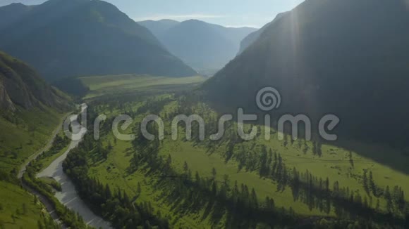 空中无人机景在日落柔和的光线下飞越松树林山河和乡村道路山区视频的预览图