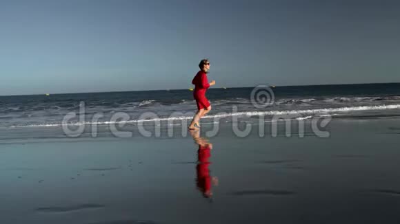 日落时分穿着红色裙子的快乐年轻女子沿着海边奔跑无忧无虑的现代生活理念视频的预览图