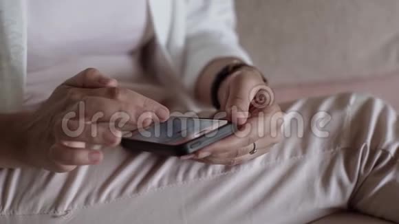 一个手里拿着智能手机的女人坐在沙发上女孩看着智能手机特写上的电子邮件视频的预览图
