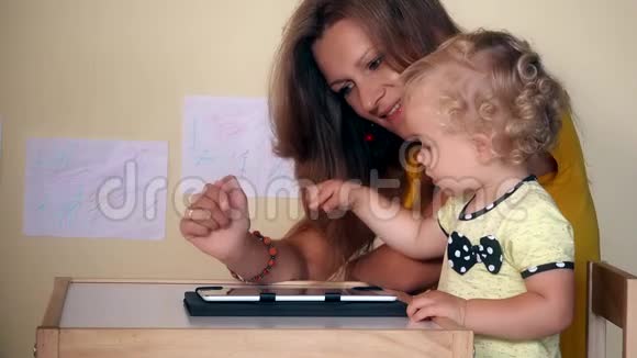 妈妈帮助她的女婴使用平板电脑坐在桌子旁视频的预览图