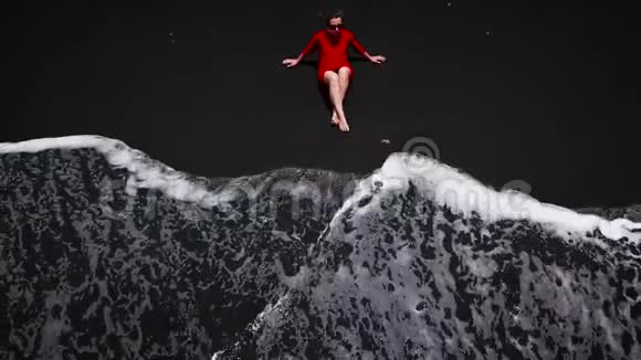 鸟瞰一个穿着红色连衣裙的女孩坐在海滩上沙滩上有黑色的沙子西班牙加那利群岛特内里费视频的预览图