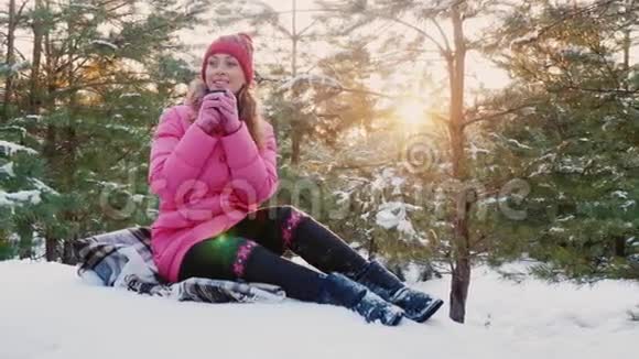 粉红色羽毛床上的年轻女人她在冬天的森林里喝茶靠近白雪覆盖的云杉和阳光视频的预览图