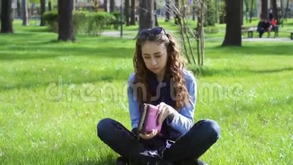 在草地上的一个夏日公园里美丽的年轻女子合上书离开了视频的预览图