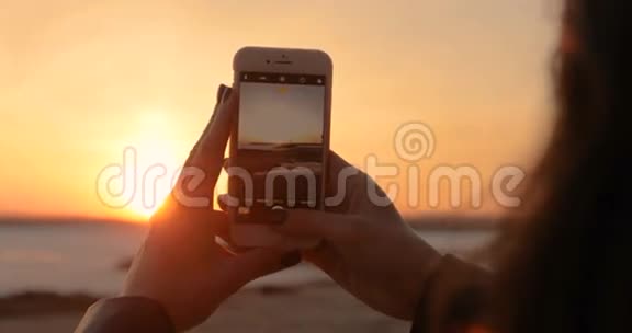 一个女孩正在智能手机上拍照日落视频的预览图