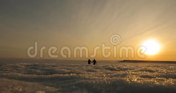 浪漫的年轻夫妇牵着手在海滩上散步太阳开始下山视频的预览图