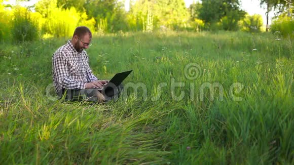 戴眼镜的快乐青年坐在草地上打字视频的预览图