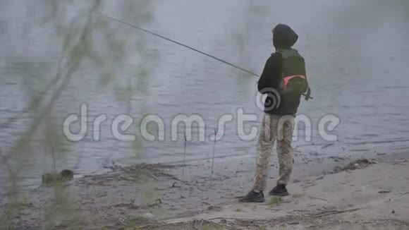 肖像年轻自信的渔夫在清晨在城市附近的河流中旋转捕鱼钓竿和鱼卷视频的预览图