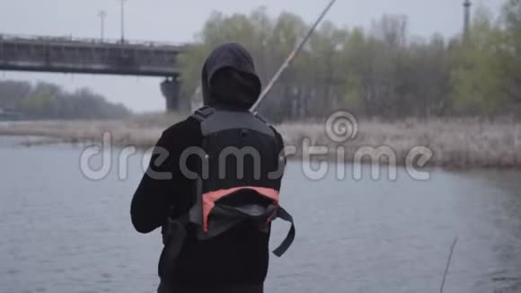 肖像年轻自信的渔夫在清晨在城市附近的河流中旋转捕鱼钓竿和鱼卷视频的预览图