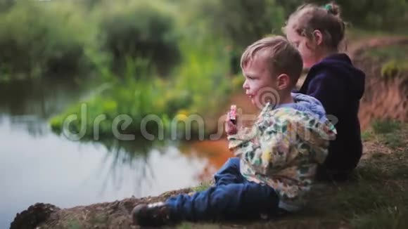 侧面看到两个可爱的小孩子一个男孩和一个女孩吃西瓜坐在河岸上视频的预览图