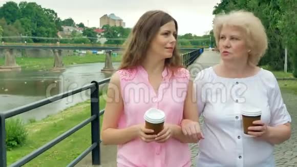 快乐的老妇人和年轻女子沿着海滨散步喝咖啡视频的预览图