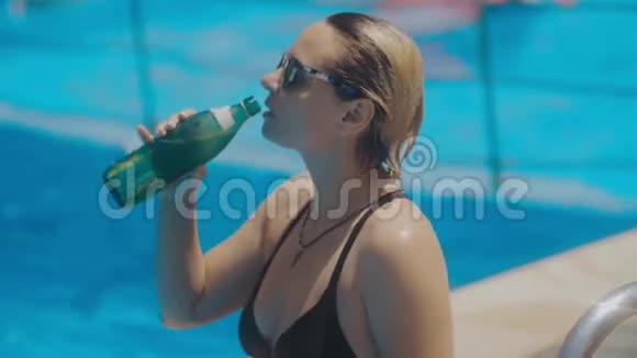 一位年轻女子在游泳池附近户外运动后喝水的特写镜头视频的预览图