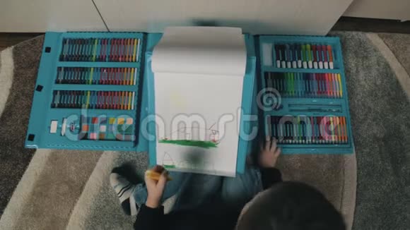 一个小男孩学会用彩色铅笔画画一个坐在地板上的男孩在一张专辑里画画视频的预览图
