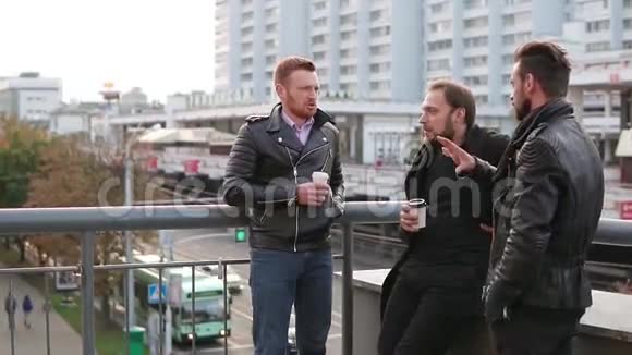 三个带胡子的年轻帅哥在桥栏杆上交谈帅哥说话喝咖啡慢节奏视频的预览图