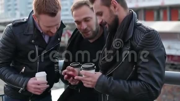 三个英俊的年轻人留着胡子微笑着自拍漂亮的男人用智能手机慢节奏视频的预览图