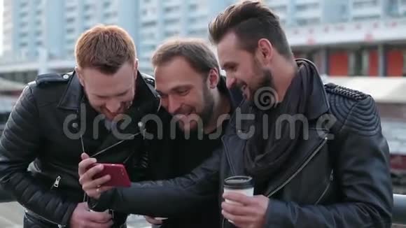 三个留着胡子的英俊青年兴高采烈地笑着漂亮的男人用智能手机慢节奏视频的预览图