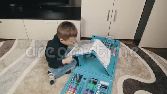 一个小男孩学会用彩色铅笔画画一个坐在地板上的男孩在一张专辑里画画视频的预览图