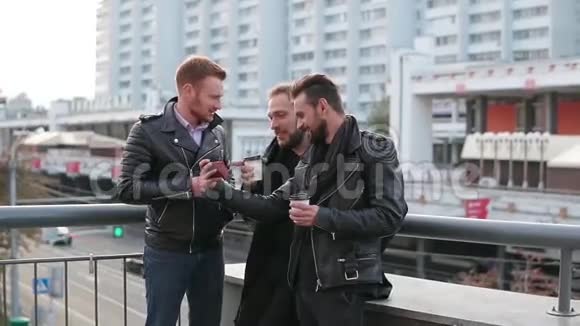 三个英俊的年轻人留着胡子用智能手机三个英俊的年轻人靠近一座桥栏杆慢节奏视频的预览图